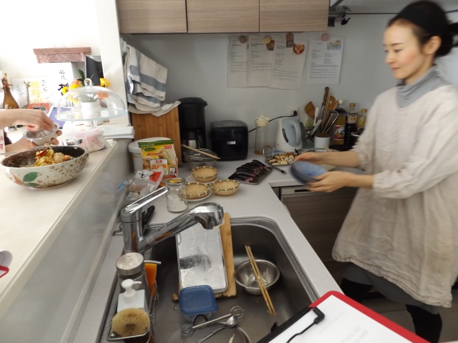 Sensei moving quickly to help get us ready to cook dishes simultaneously. Spy salmon in vinegar in the bowl on the left on the counter.