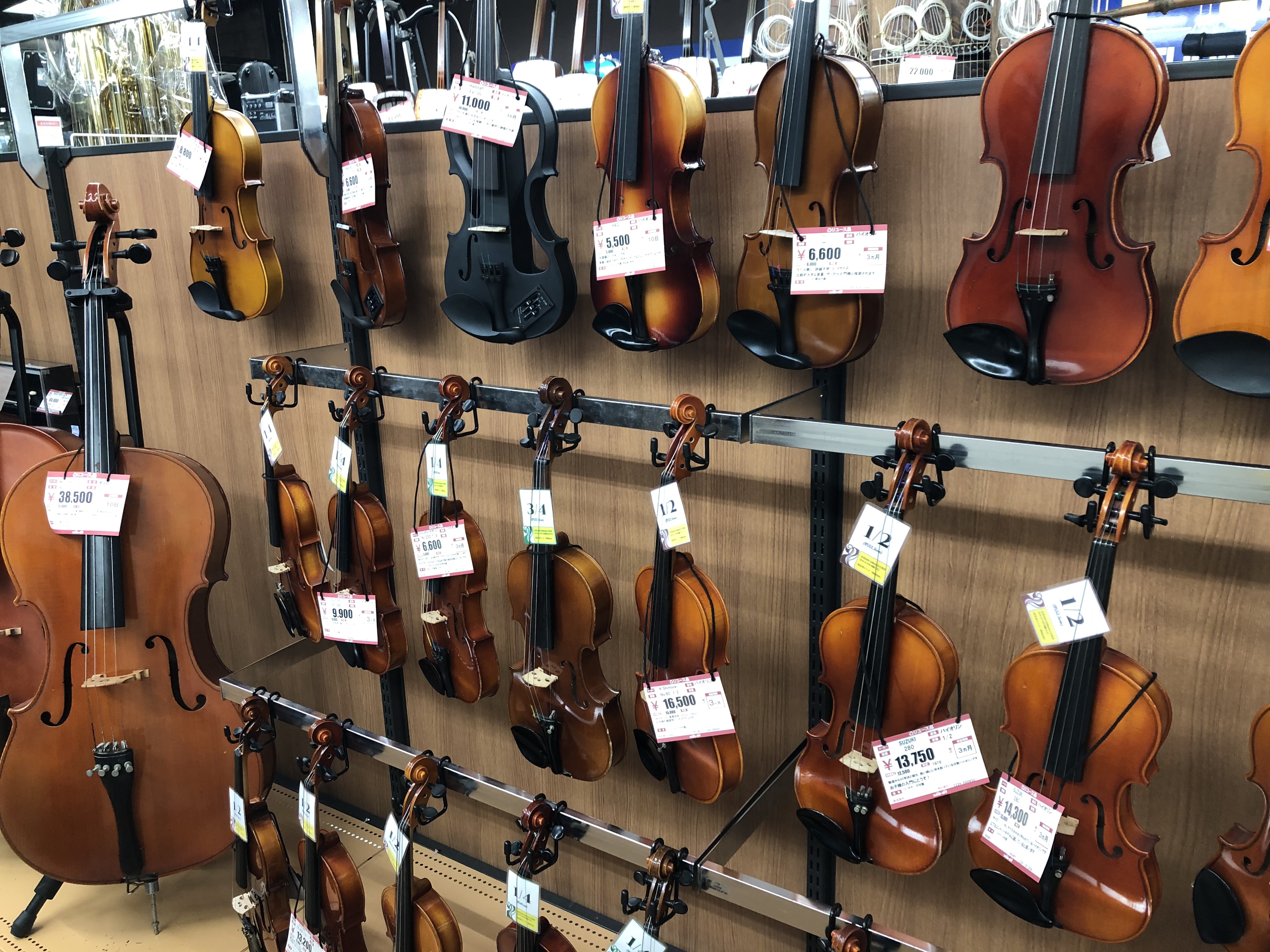 Second-hand violins, violas and cellos line the wall in the instruments floor of Hard Off, a recycle shop in Tokyo. Photo by Denisse Rauda